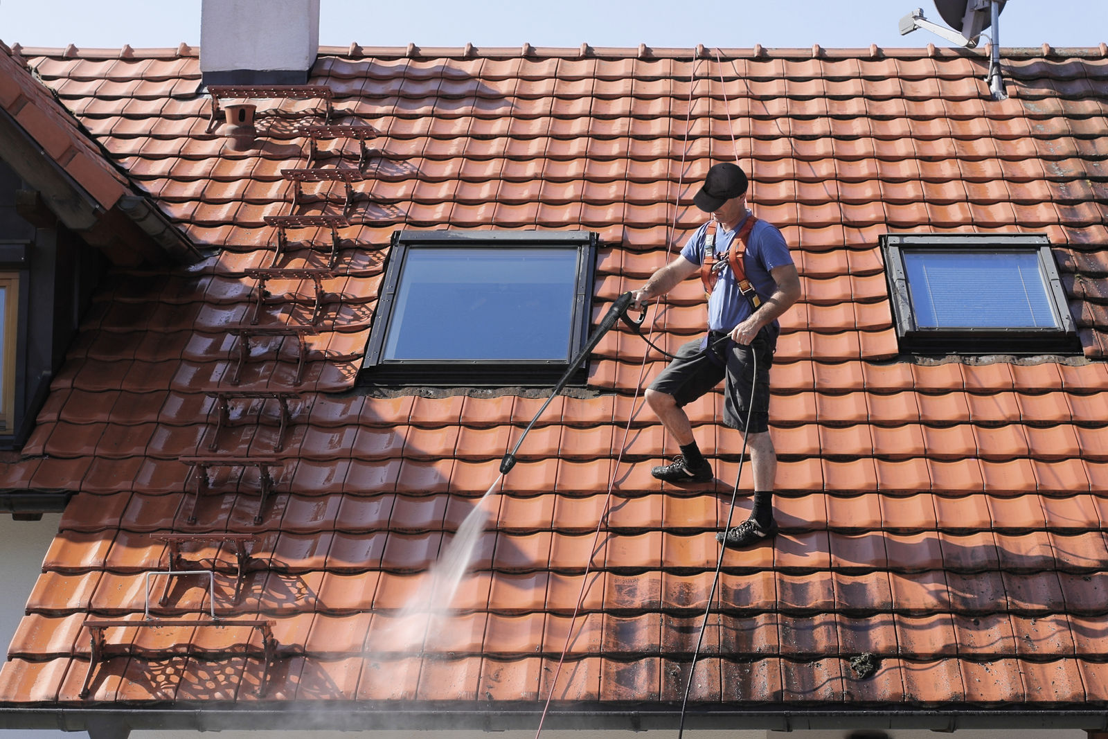 Worker soft washing a residential tile roof